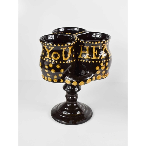 173 - A terracotta treacle glazed puzzle cup, with slip ware inscription 'Here is a Heath to you', 22cm hi... 