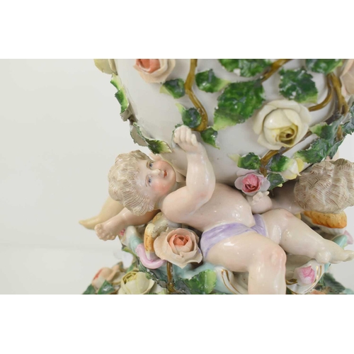 223 - A German porcelain oil lamp, the body modelled with cherubs and flowers.