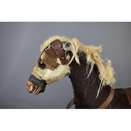 351 - An antique child's play horse / pulley horse, clad in pony skin, leather saddle and glass eyes, rais... 