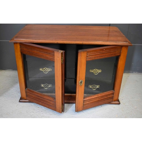 499 - An Edwardian mahogany collectors cabinet with ebonised interior drawers enclosed by glass doors.