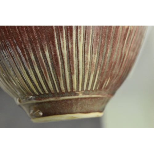 100 - Bridget Drakeford (b.1946): A maroon glazed jug with vertical striped pattern and knot form handle t... 