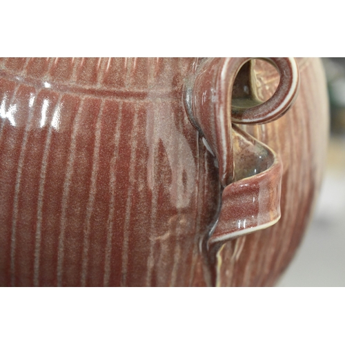 100 - Bridget Drakeford (b.1946): A maroon glazed jug with vertical striped pattern and knot form handle t... 