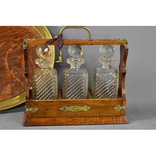 250 - A Victorian oak cased tantalus, with three cut glass decanters, the case clad with brass and having ... 