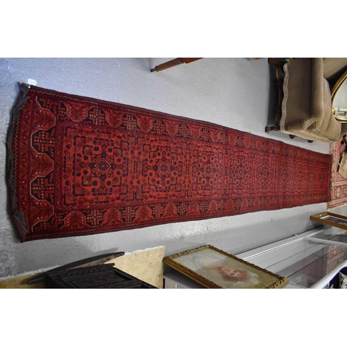 255 - A very long wool runner, the red ground with geometric stylised motifs 81 by 500cm.