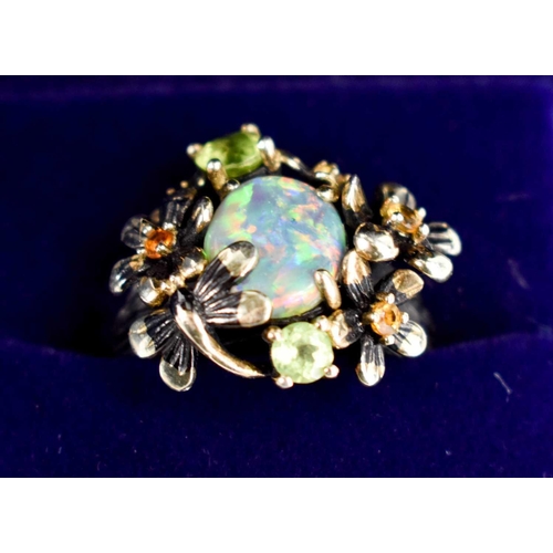 162 - An oval opal, silver and peridot set ring, the branch form shank forming butterflies and flowerheads... 