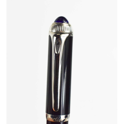 57 - A Cartier ballpoint pen, black composite body and cap, palladium-finish details, blue resin cabochon... 