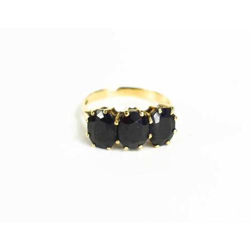 85 - A 9ct gold and dark sapphire three stone ring, each of the oval cut almost black sapphires of approx... 