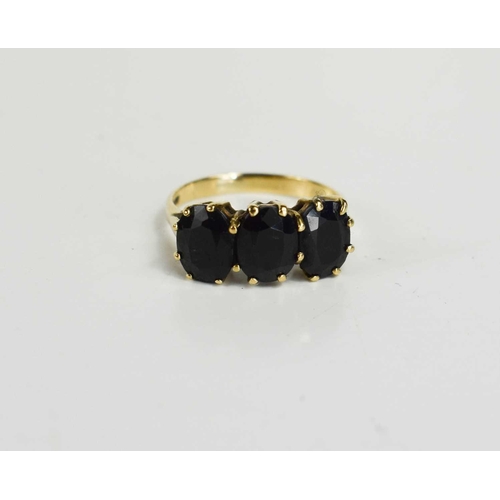 85 - A 9ct gold and dark sapphire three stone ring, each of the oval cut almost black sapphires of approx... 