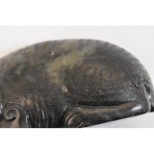 107 - A Qing Dynasty black jade mythical beast, of large pebble form, shown crouched with the legs folded ... 