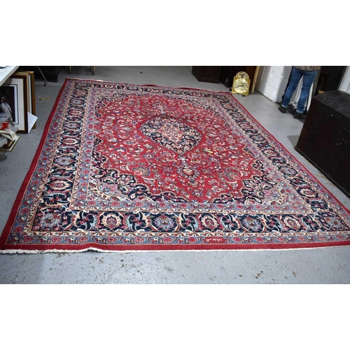 607 - A large Middle Eastern red ground rug with stylised floral motifs to the centre and repeating border... 