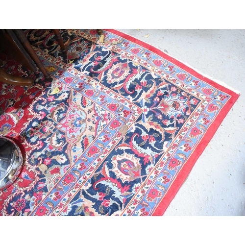 607 - A large Middle Eastern red ground rug with stylised floral motifs to the centre and repeating border... 