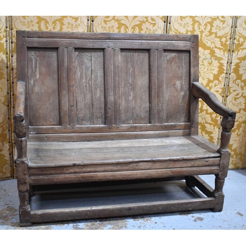 660 - An 18th century oak or elm settle, the high back having a four panel backrest and shaped open arms, ... 