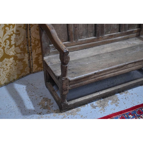 660 - An 18th century oak or elm settle, the high back having a four panel backrest and shaped open arms, ... 