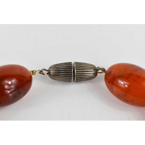 140 - A red amber beaded necklace, the oval beads measure approximately 2.5cm long, with a screw clasp, en... 