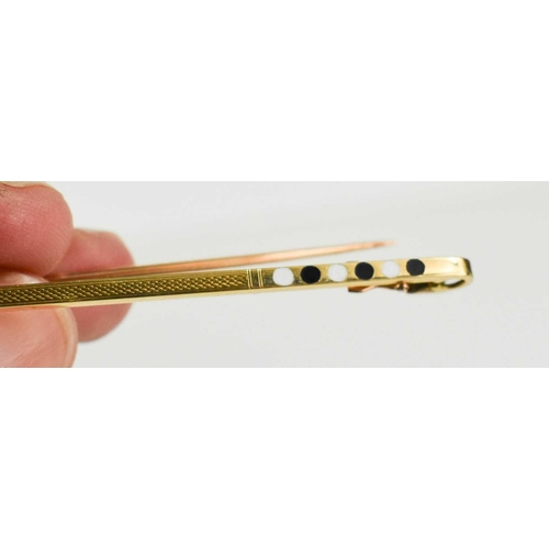 67 - A 14k gold and enamel bar brooch, the machine engraved central area flanked by black and white ename... 