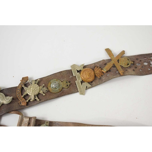 38 - A vintage leather belt adorned with various regimental cap badges, including the Royal Sussex, The D... 