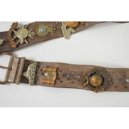 38 - A vintage leather belt adorned with various regimental cap badges, including the Royal Sussex, The D... 