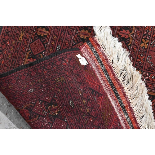 458 - A large deep red rug, possibly Bokhara, the central ground with repeating guls, and having a deep bo... 