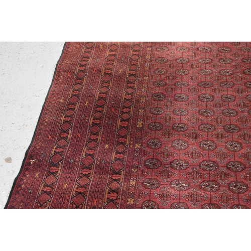 458 - A large deep red rug, possibly Bokhara, the central ground with repeating guls, and having a deep bo... 