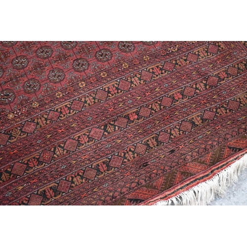 458 - A large deep red rug, possibly Bokhara, the central ground with repeating guls, and having a deep bo... 