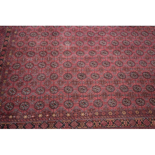 458 - A large deep red rug, possibly Bokhara, the central ground with repeating guls, and having a deep bo... 