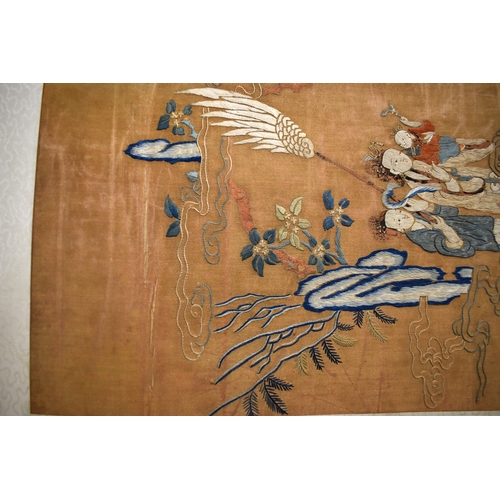 492 - A Chinese scroll with silk embroidered panel depicting two women holding a baby, with gentleman gest... 