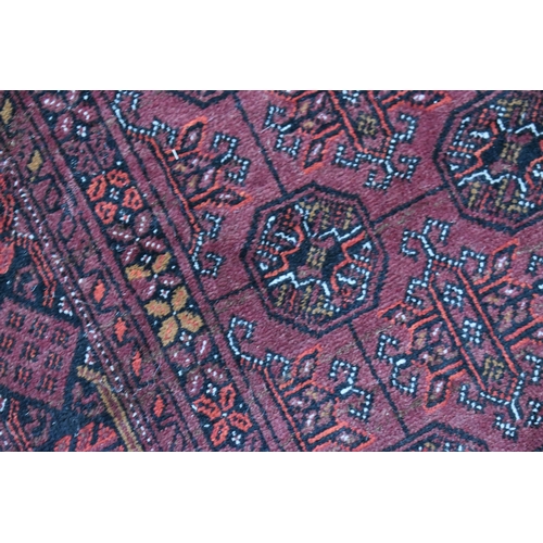 458 - A large deep red rug, possibly Bokhara, the central ground with repeating guls, and having a deep bo... 