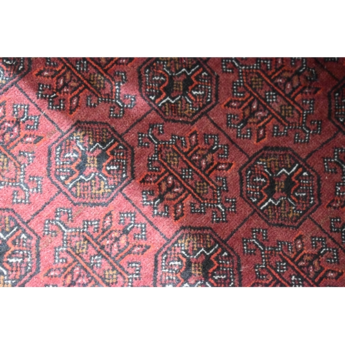 458 - A large deep red rug, possibly Bokhara, the central ground with repeating guls, and having a deep bo... 