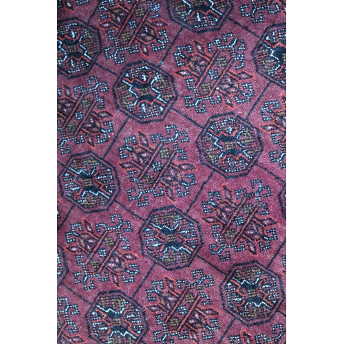 458 - A large deep red rug, possibly Bokhara, the central ground with repeating guls, and having a deep bo... 