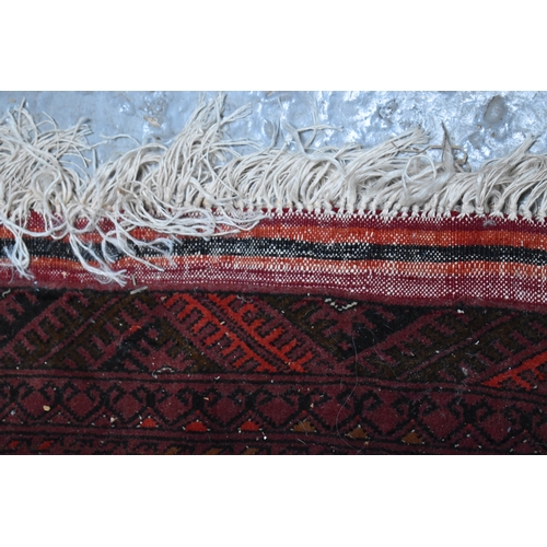 458 - A large deep red rug, possibly Bokhara, the central ground with repeating guls, and having a deep bo... 