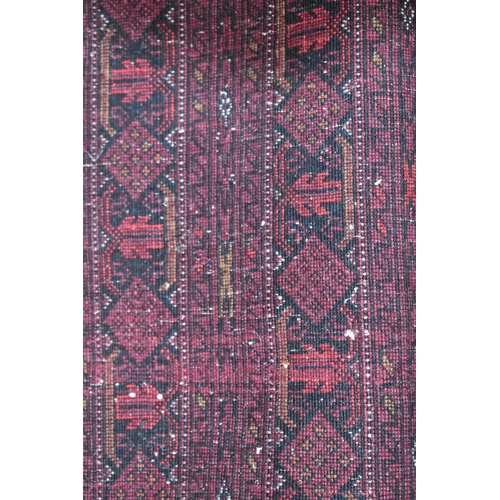 458 - A large deep red rug, possibly Bokhara, the central ground with repeating guls, and having a deep bo... 