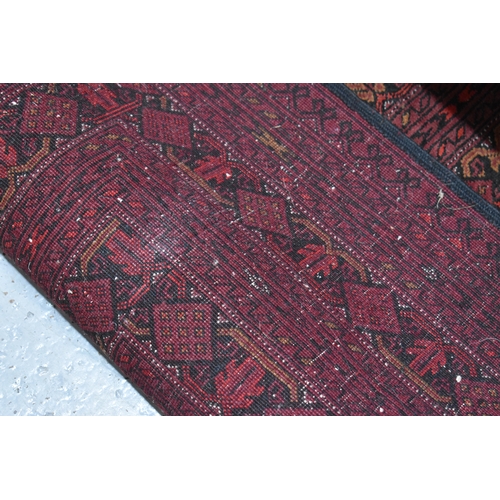 458 - A large deep red rug, possibly Bokhara, the central ground with repeating guls, and having a deep bo... 