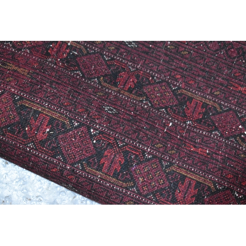 458 - A large deep red rug, possibly Bokhara, the central ground with repeating guls, and having a deep bo... 