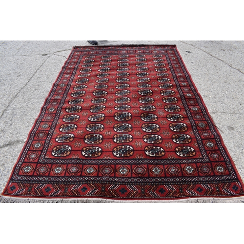 452a - A Middle Eastern Bokhara wool rug, red ground with repeating geometric patterns, 200cm by 300cm.