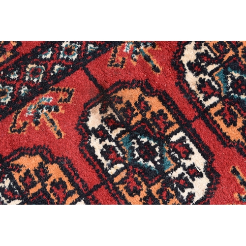 452a - A Middle Eastern Bokhara wool rug, red ground with repeating geometric patterns, 200cm by 300cm.