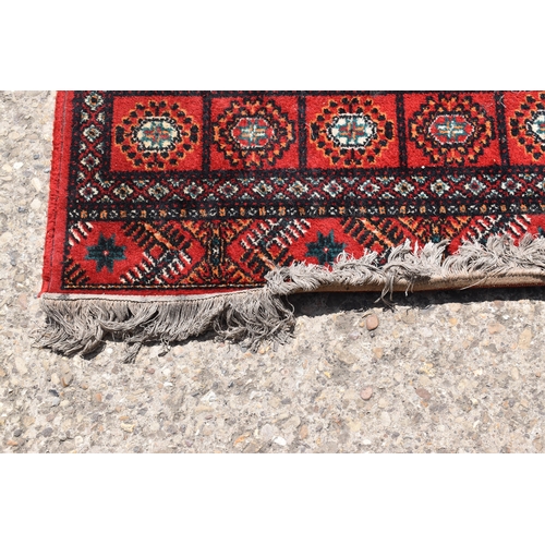 452a - A Middle Eastern Bokhara wool rug, red ground with repeating geometric patterns, 200cm by 300cm.