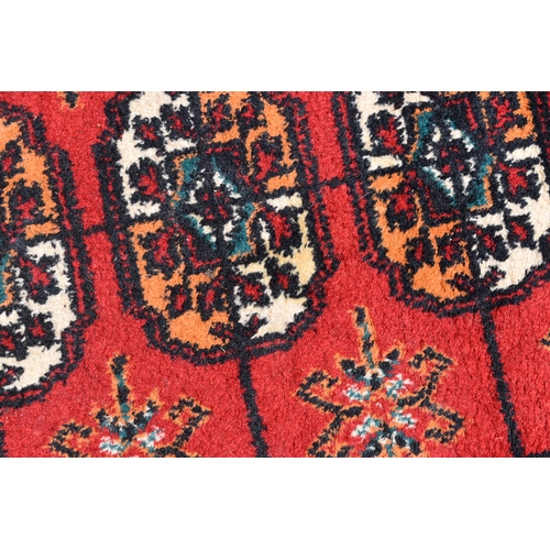 452a - A Middle Eastern Bokhara wool rug, red ground with repeating geometric patterns, 200cm by 300cm.