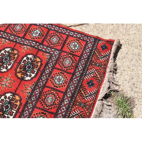 452a - A Middle Eastern Bokhara wool rug, red ground with repeating geometric patterns, 200cm by 300cm.