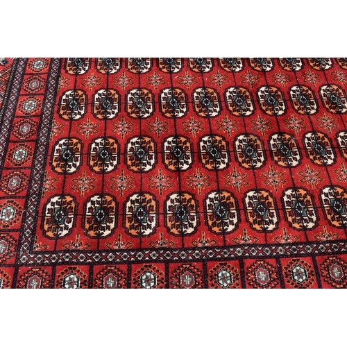 452a - A Middle Eastern Bokhara wool rug, red ground with repeating geometric patterns, 200cm by 300cm.