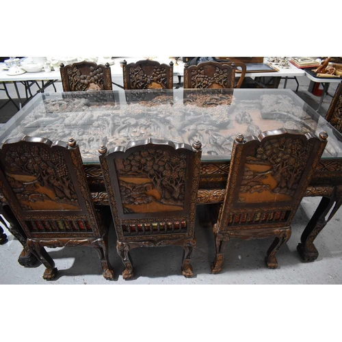 118 - A large carved Oriental hardwood dining table with glass top, the carvings depicting figures and arc... 