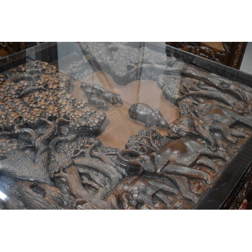 118 - A large carved Oriental hardwood dining table with glass top, the carvings depicting figures and arc... 