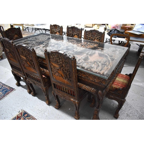 118 - A large carved Oriental hardwood dining table with glass top, the carvings depicting figures and arc... 