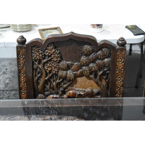 118 - A large carved Oriental hardwood dining table with glass top, the carvings depicting figures and arc... 