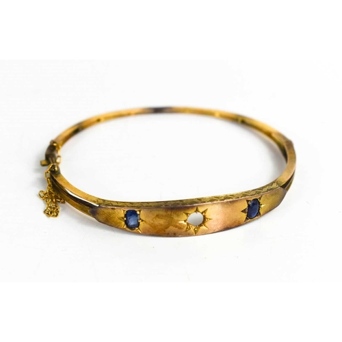 189 - A 9ct gold and sapphire bangle, the two oval cut sapphires approximately ¼ct each, (lacking central ... 