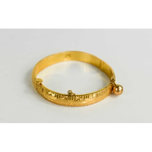 258 - A Chinese gold bangle, embossed with decoration and having a single bell, screw form clasp, unmarked... 