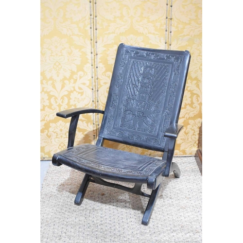 398 - An early 20th century ebonised Chinese folding armchair with leather back and seat embossed with sty... 