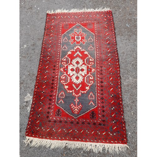 82 - Red ground hand knotted rug with long blue central motif, 185cm x 85cm