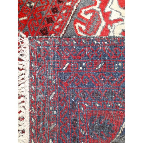 82 - Red ground hand knotted rug with long blue central motif, 185cm x 85cm