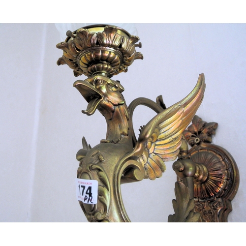 174 - Pair of ornate brass wall lights with winged serpent decoration, shaped shades, on backplates