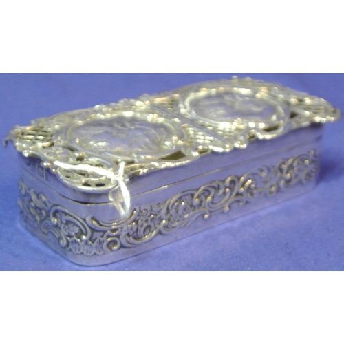 192 - Ornate London silver ring box with cherub decorated pierced top and scroll decoration. H3cm x 11x 5c... 